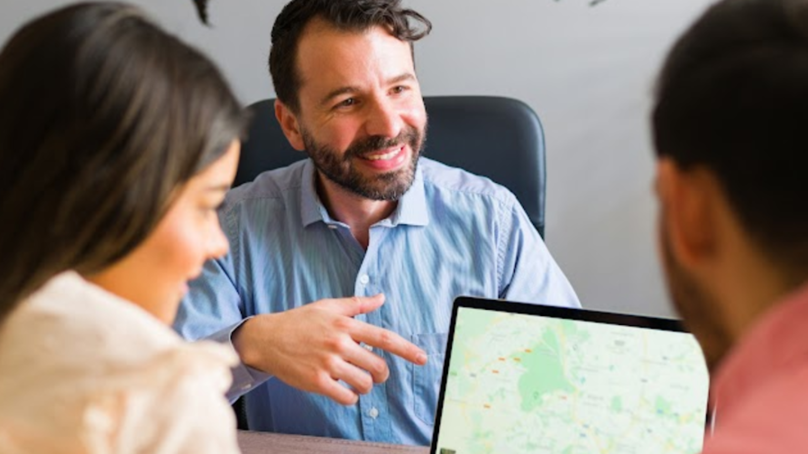 Travel agent consulting clients using travel agency software with digital maps and booking tools.