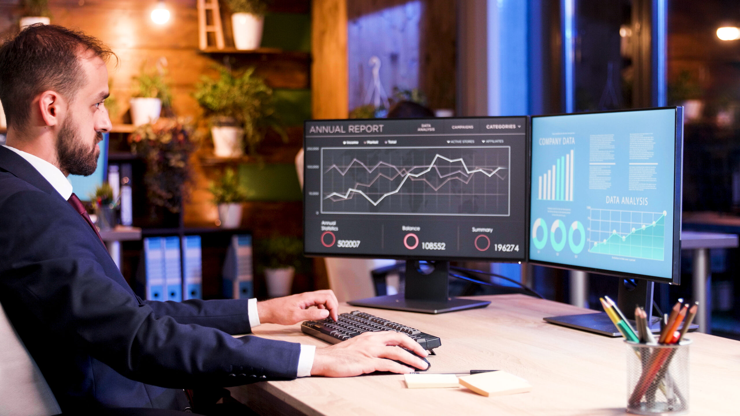 Business professional analyzing data on dual monitors using B2B Travel Software with real-time dashboards and analytics in a modern office setting.